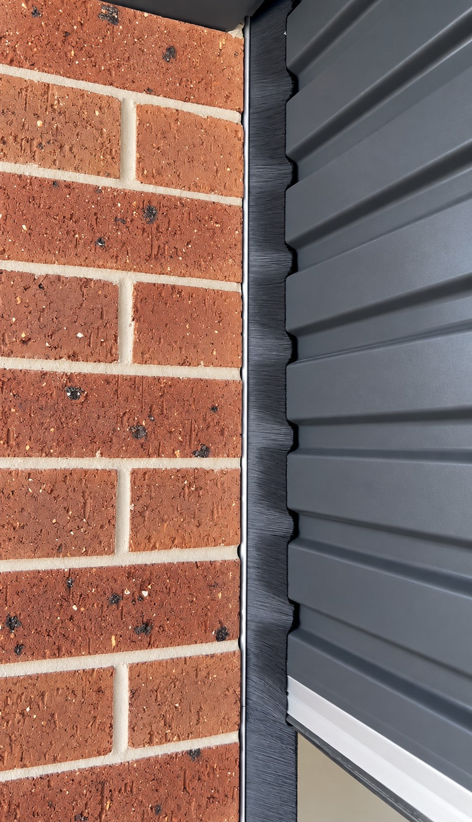 A brush side seal fitted to a Colorbond roller door, closing the gap against the brickwork