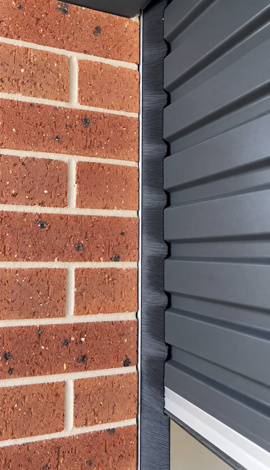 Brush side seal fitted to a Colorbond roller door against red brickwork
